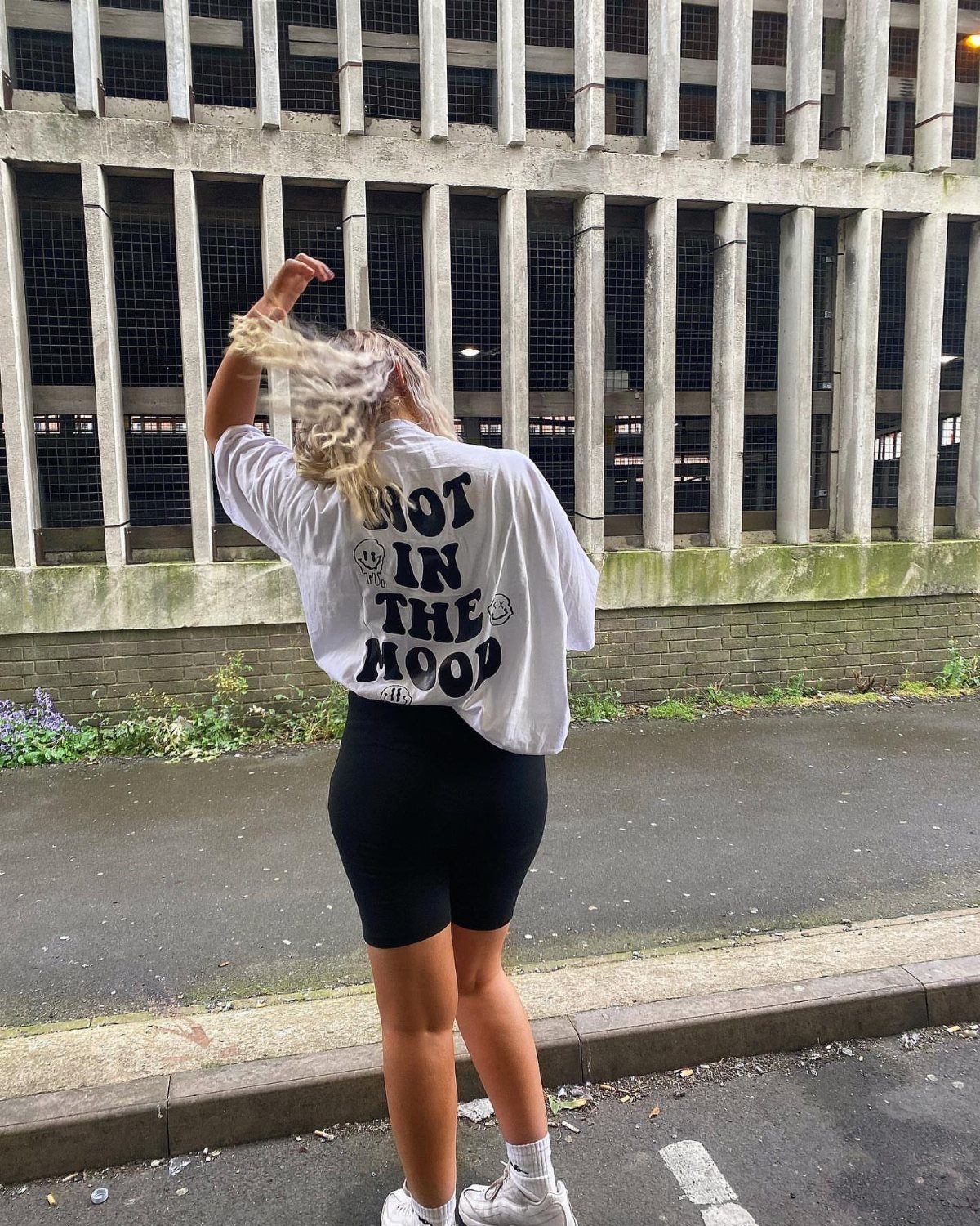 3 Modest Rave Outfits That Keep You Covered and Comfortable 1 Person wearing an oversized white graphic t-shirt and black cycling shorts from behind.