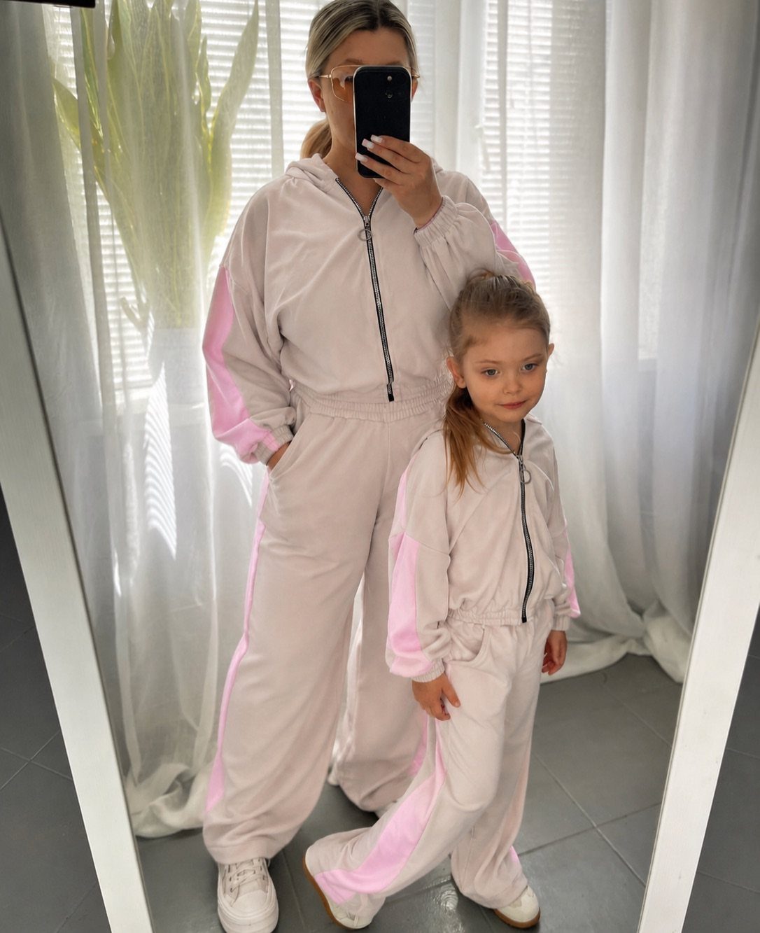 Mom and Daughter Matching Outfits for Every Occasion (6) 3 Woman and young daughter wearing matching light pink athletic tracksuits posing for mirror selfie.