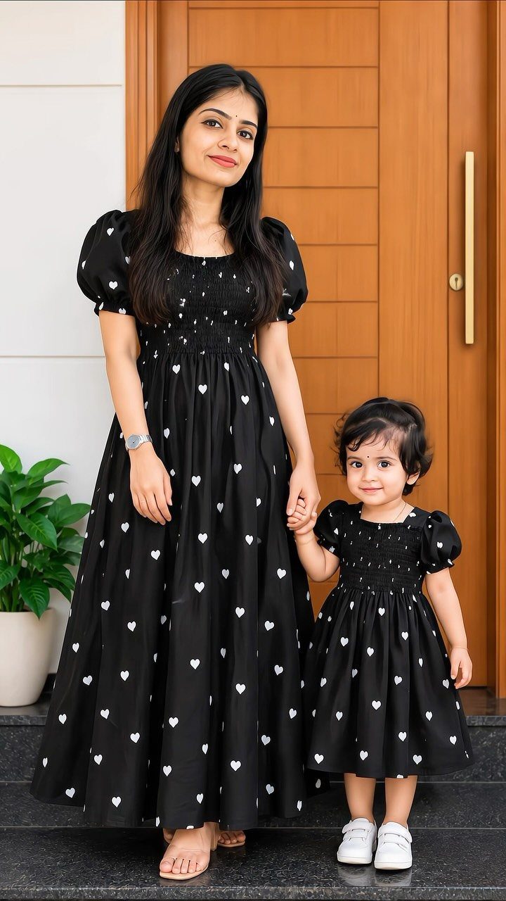 Mom and Daughter Matching Outfits for Every Occasion (6) 1 Woman and young daughter wearing matching black dresses with white heart patterns.