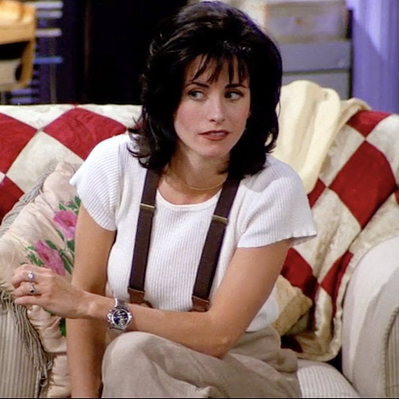Monica Geller Outfits: 8 Iconic Looks to Recreate Now 4 Woman wearing white ribbed t-shirt and brown suspenders sitting on checkered sofa.