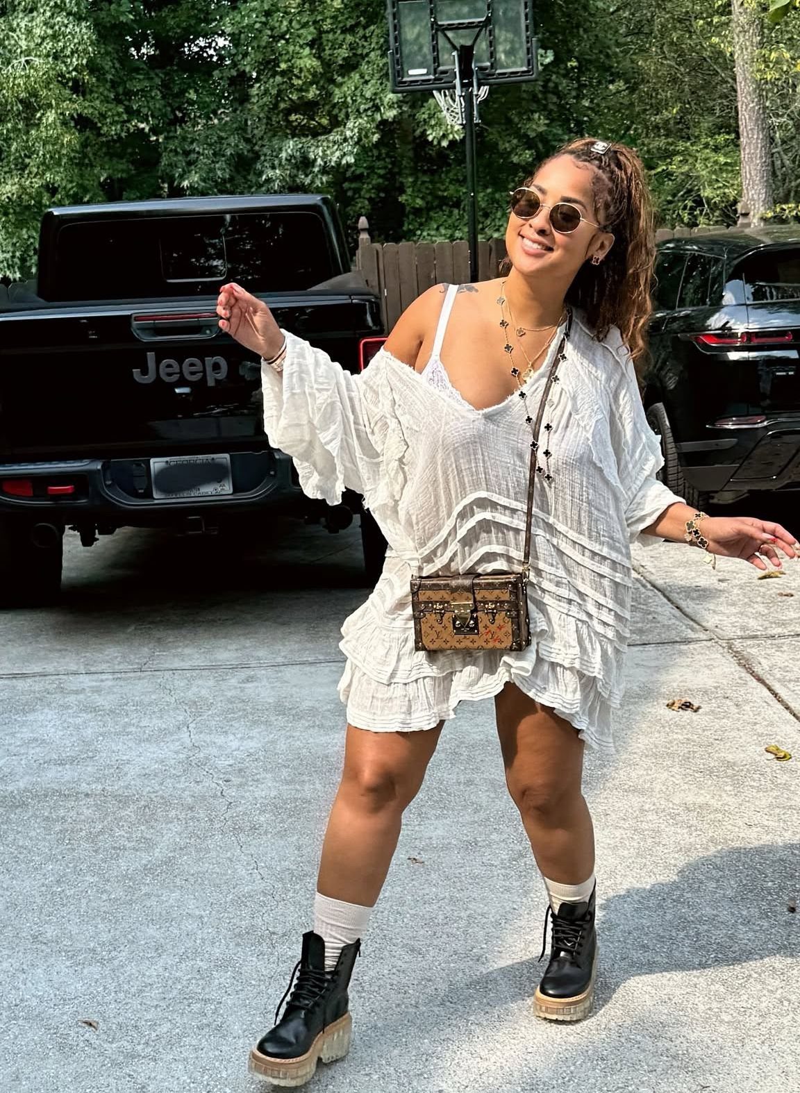 9 Music Festival Outfits for Every Weather and Vibe in 2026 3 Woman in white cotton dress with shoulder bag and chunky black boots posing outdoors.