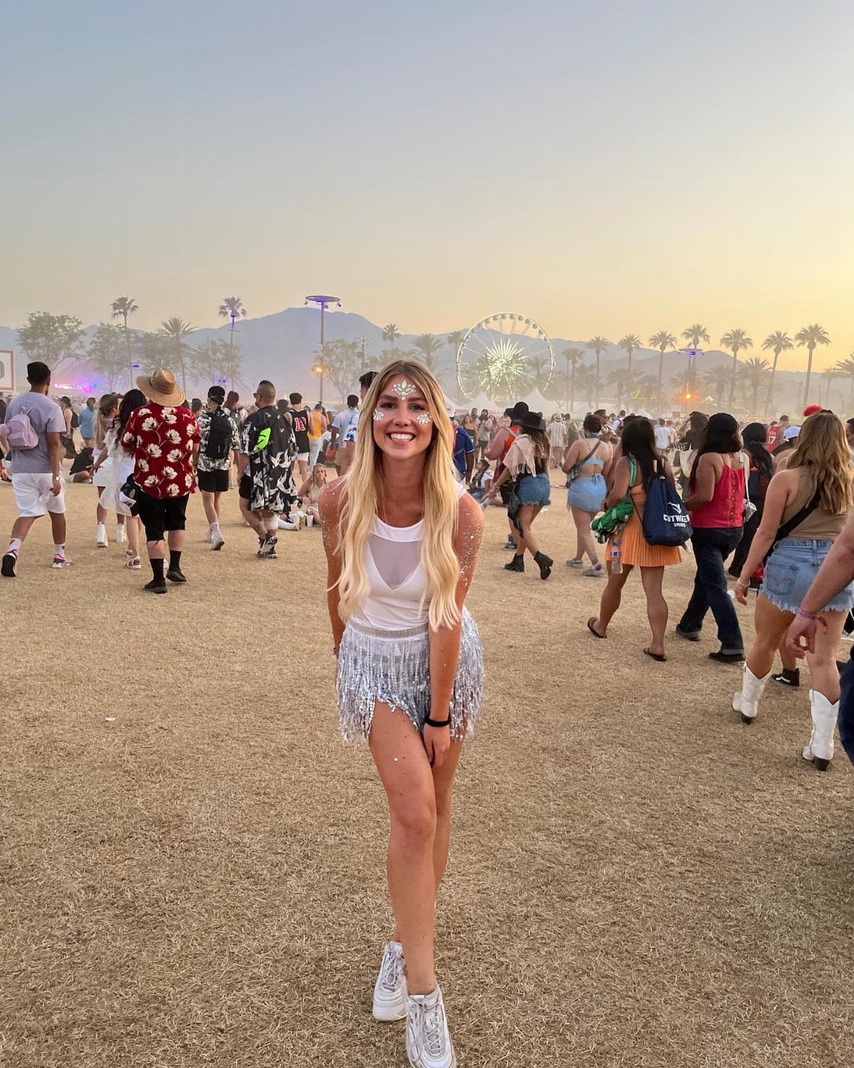 9 Music Festival Outfits for Every Weather and Vibe in 2026 8 Woman in white tank top and silver fringe skirt at outdoor music festival.