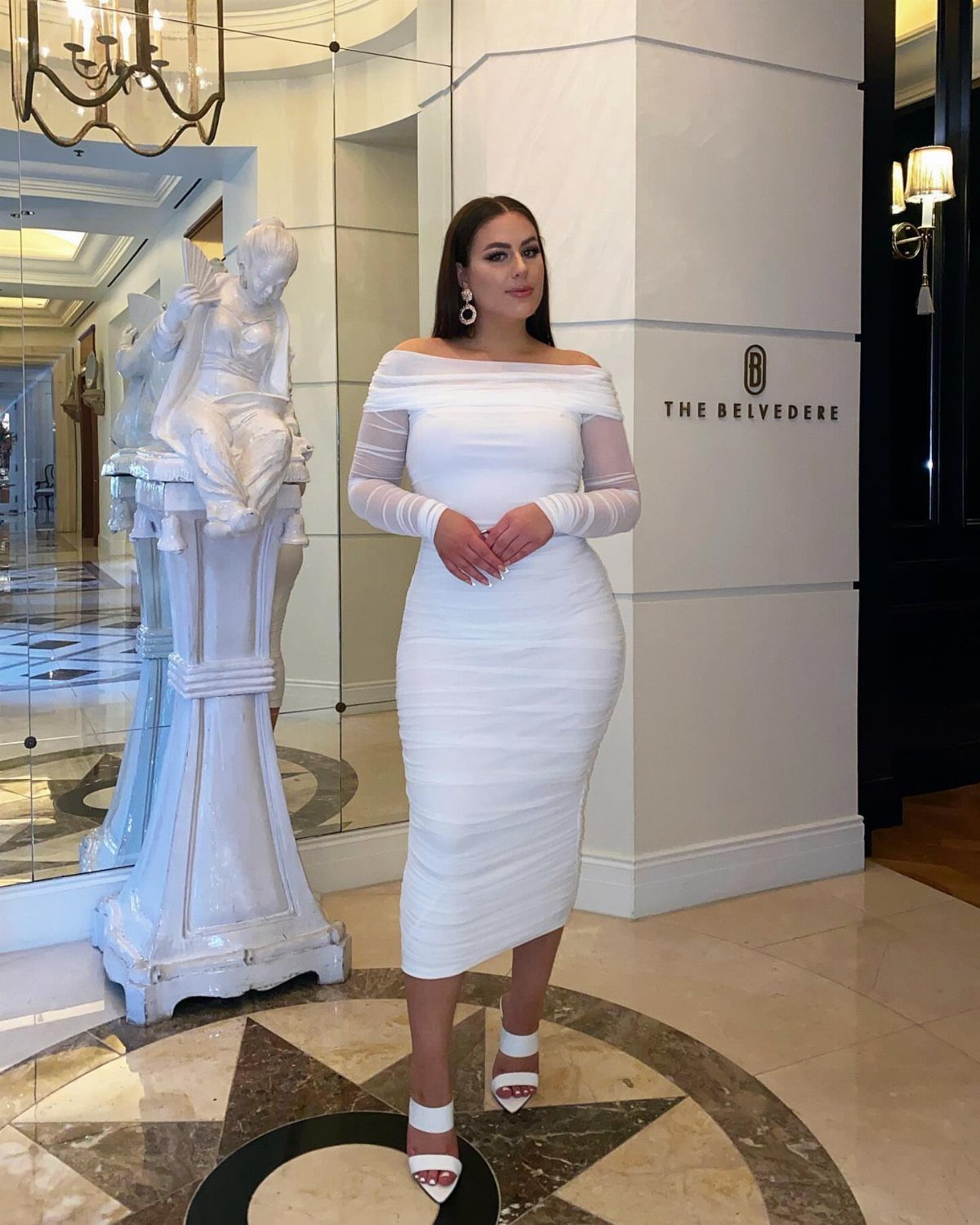 Off Shoulder Outfits: 8 Ideas from Casual to Dressed Up 1 Woman in a white off-the-shoulder midi dress posing in a luxury hotel lobby.