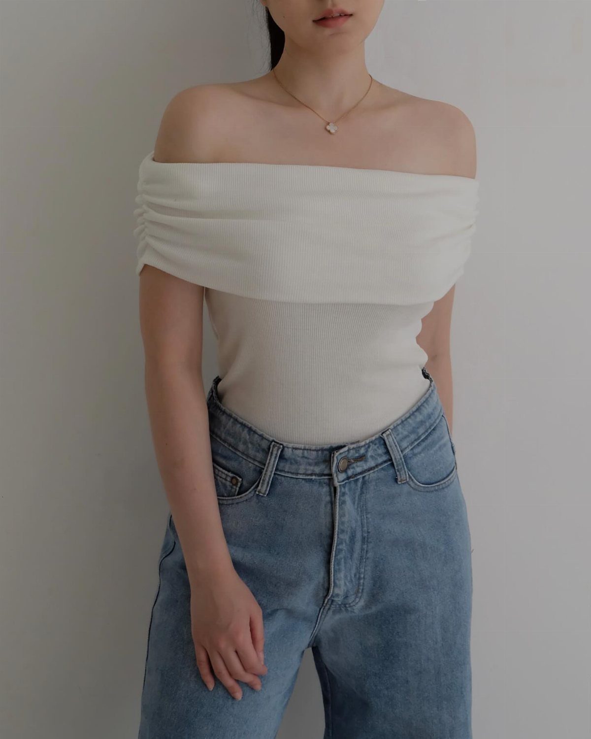 Off Shoulder Outfits: 8 Ideas from Casual to Dressed Up 6 Person wearing a white off-the-shoulder ribbed top and high-waisted blue jeans.