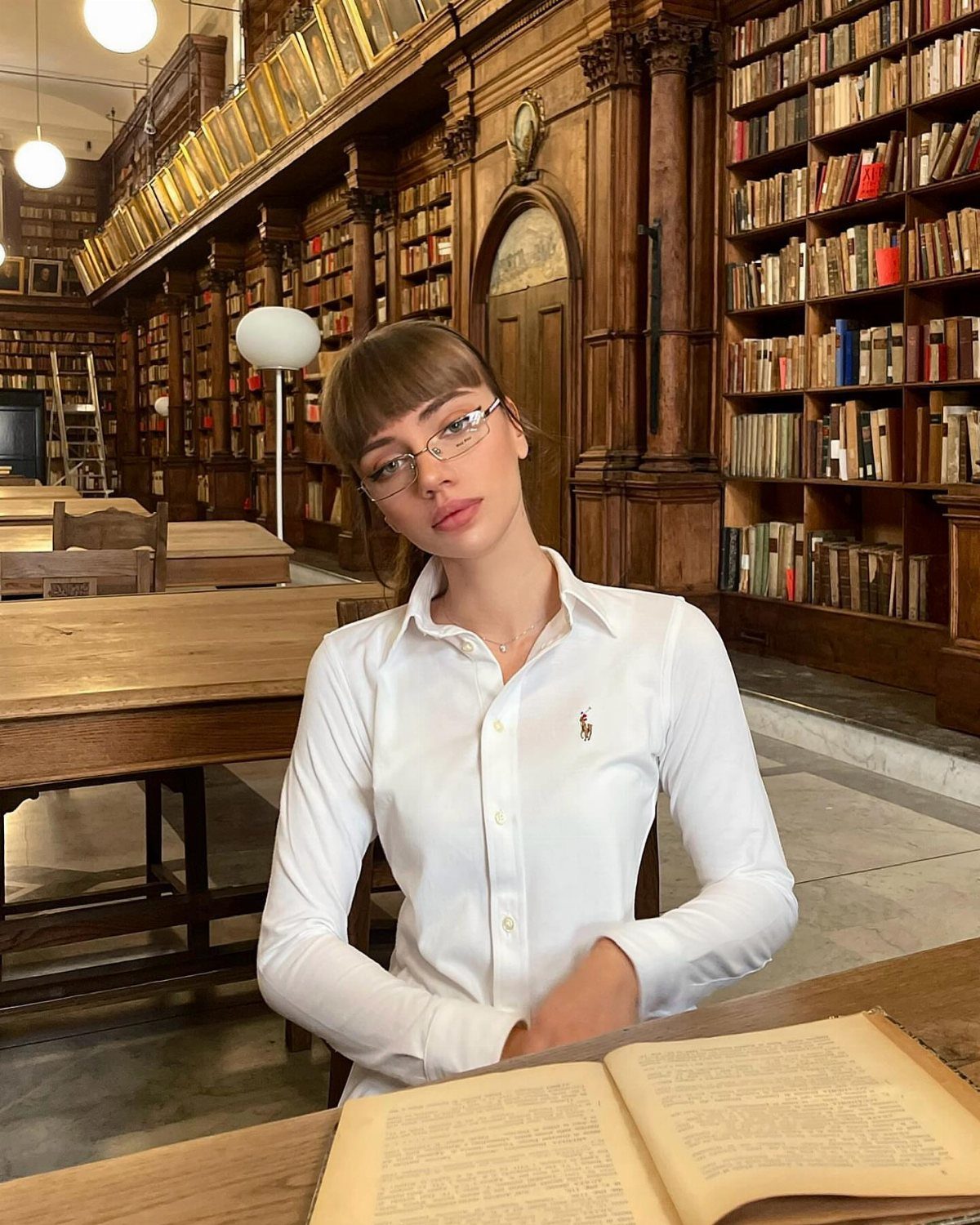 8 Office Siren Outfits to Master the Look in 2026 6 Woman in white button-down shirt and glasses posing in a vintage library.