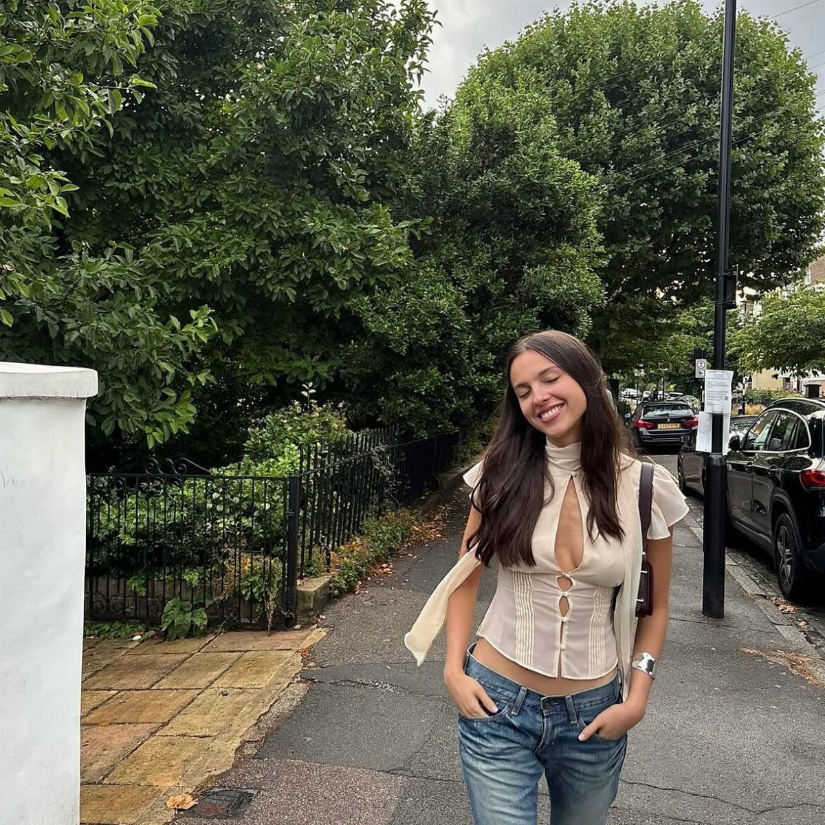 Olivia Rodrigo wearing a cream corset top and distressed blue jeans on a sidewalk