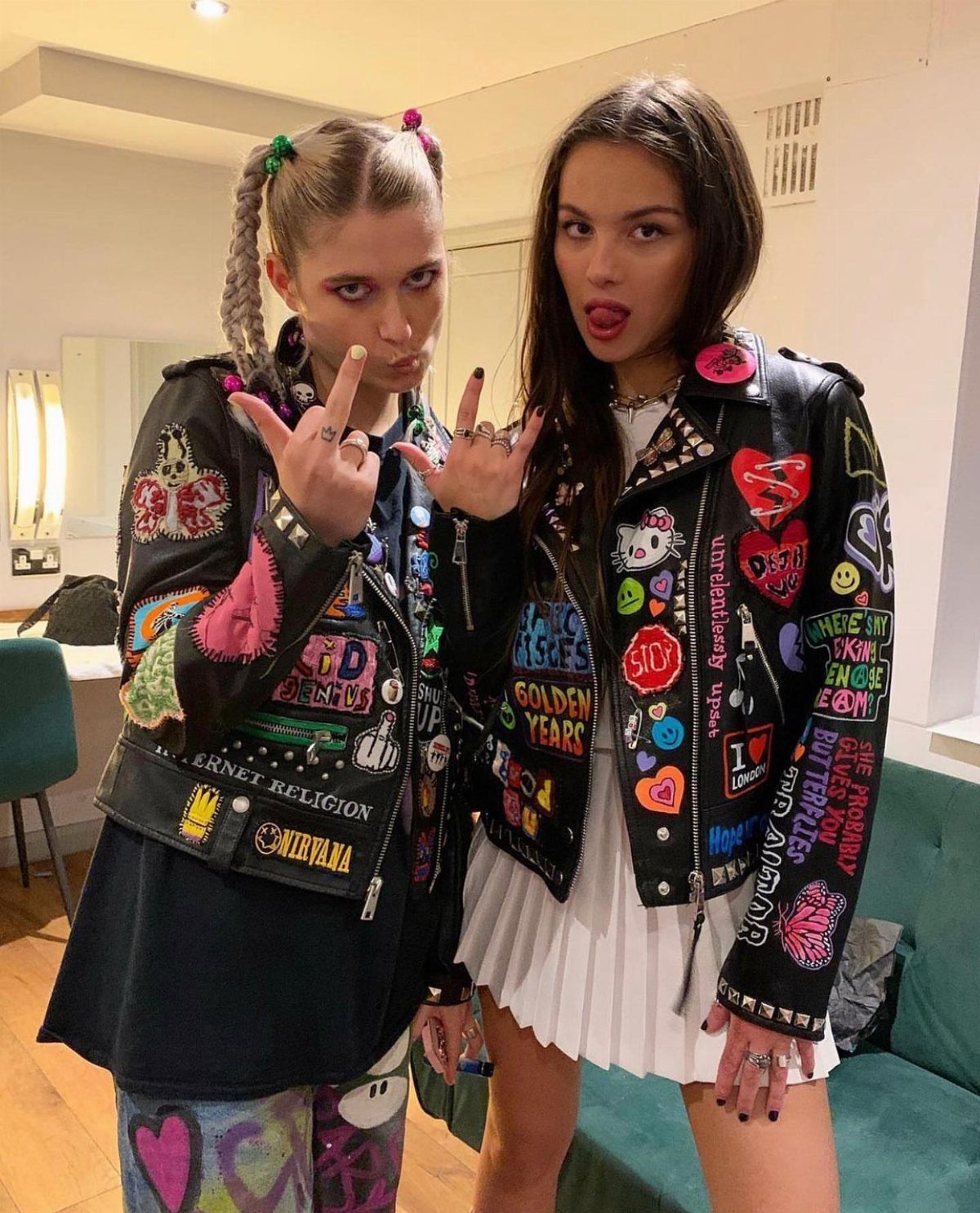 Two women wearing patch-covered leather jackets and edgy streetwear posing indoors.