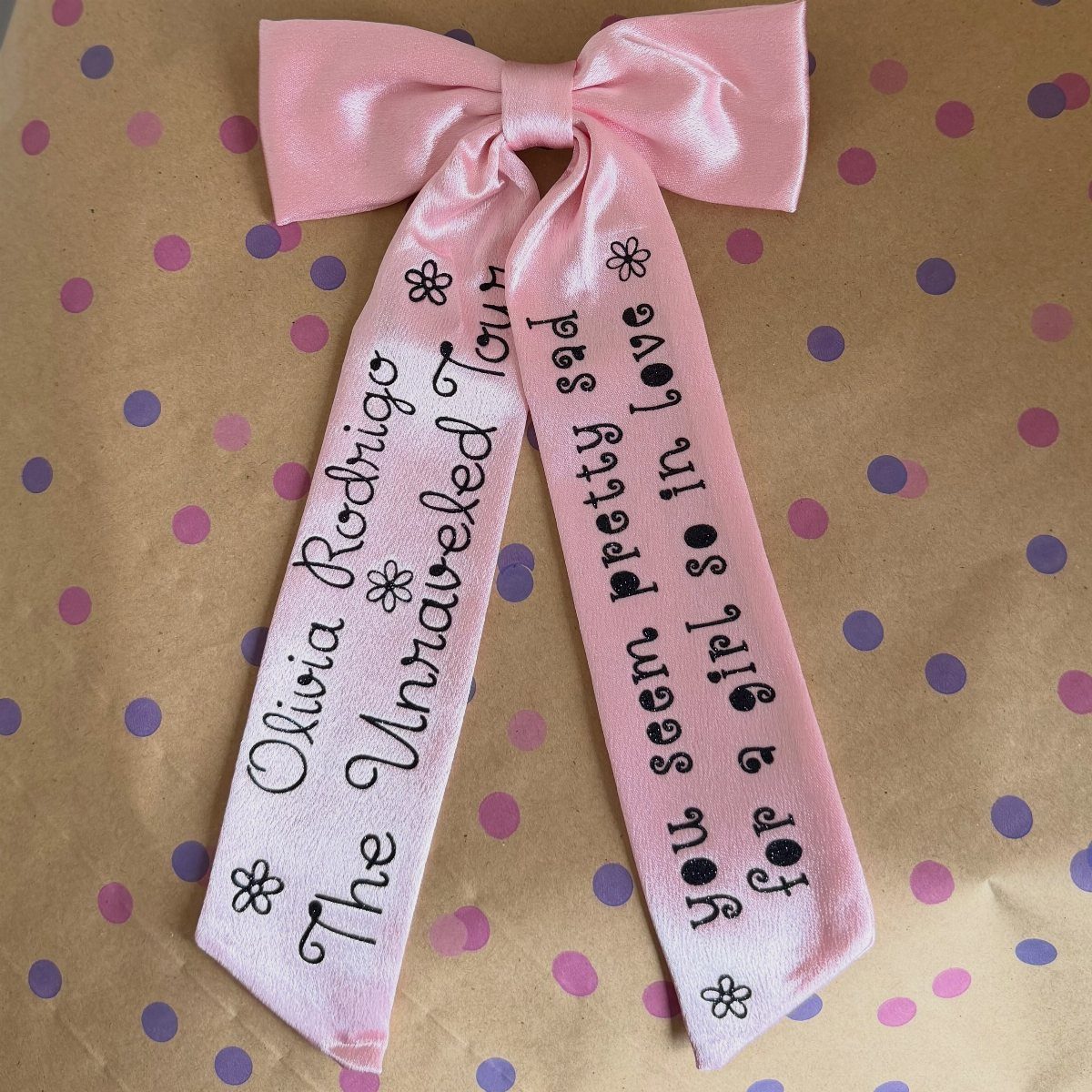 Pink satin ribbon bow with Olivia Rodrigo tour text on polka dot paper