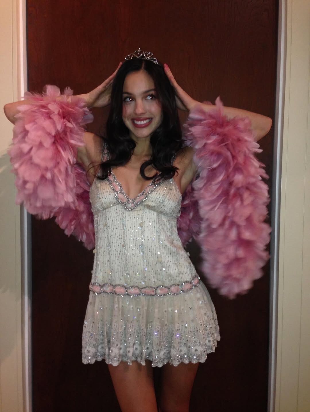 Young woman in a sparkling white dress with a pink feather boa and tiara.