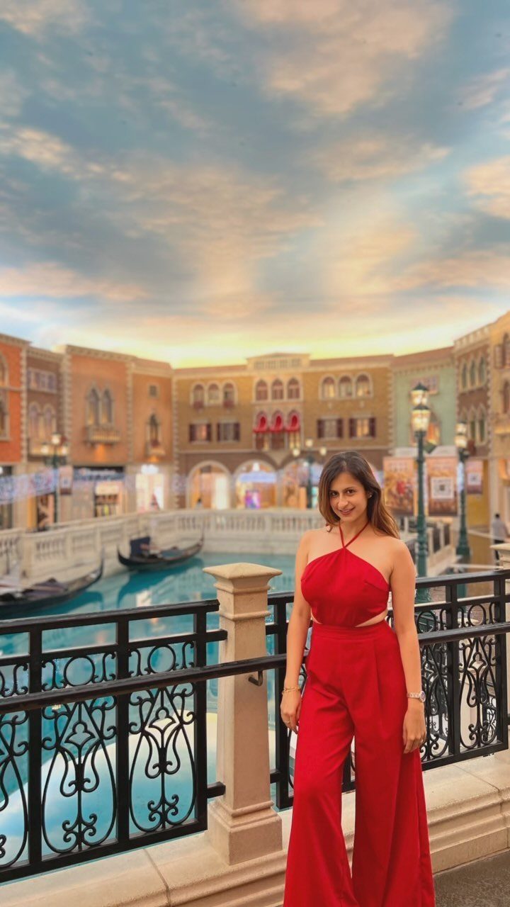 Woman in a red wide-leg jumpsuit posing on a bridge by a canal.