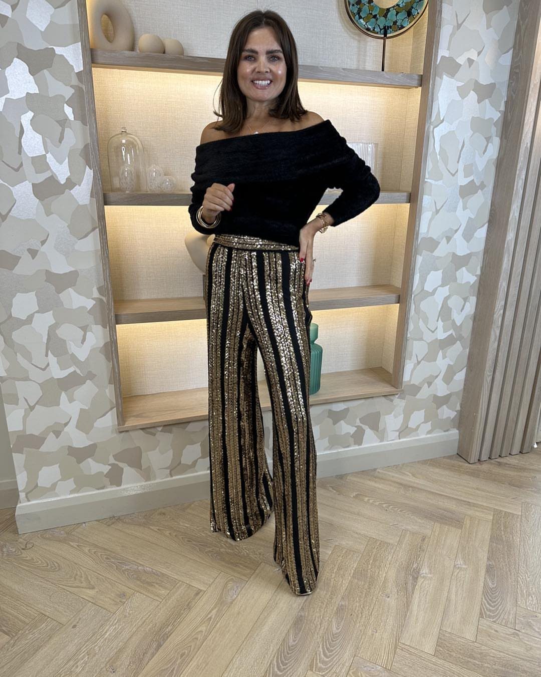 Woman wearing black velvet top and gold sequined wide-leg palazzo pants indoors.