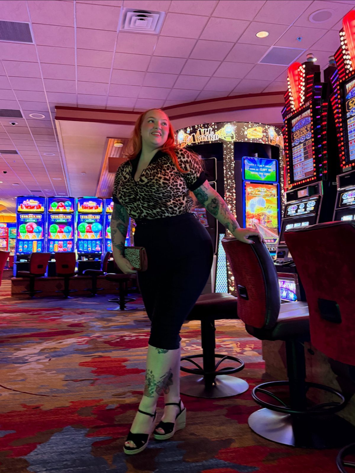 Woman in leopard print shirt and black skirt posing inside a brightly lit casino.