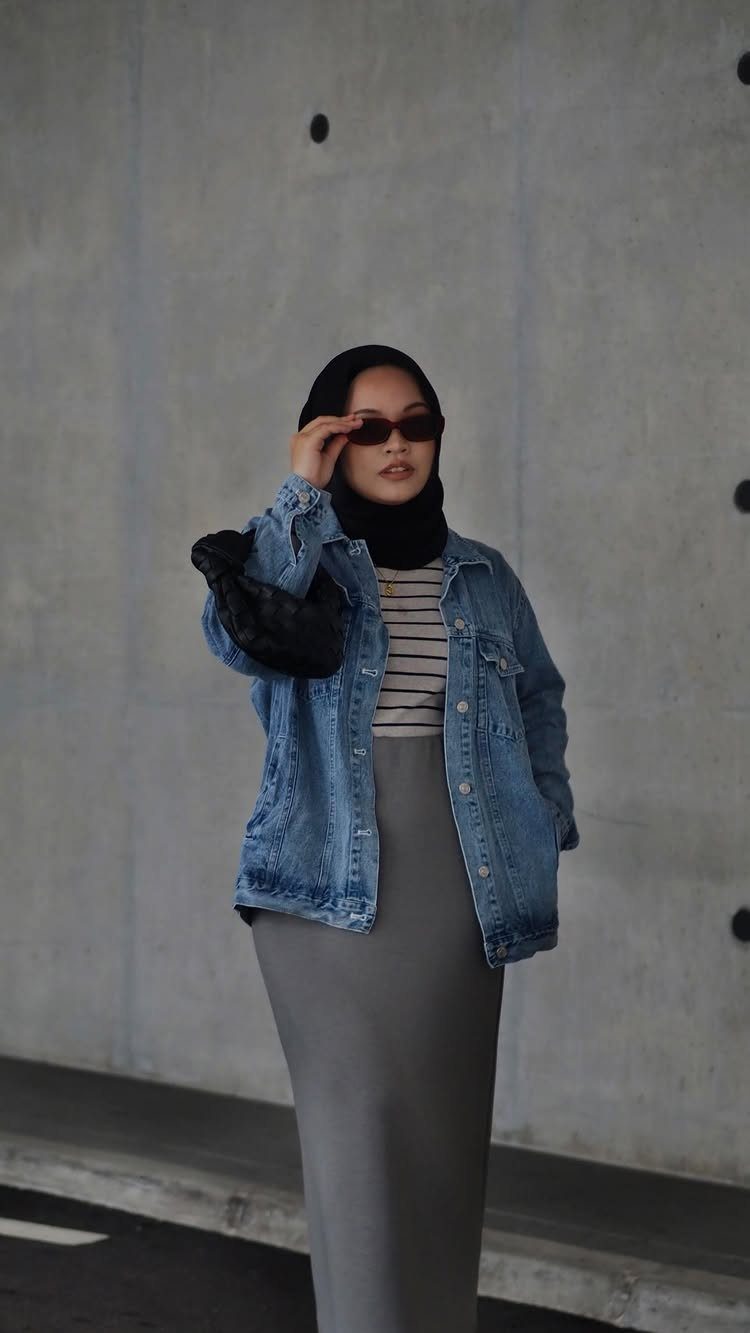 Woman in a grey pencil skirt and blue denim jacket posing against concrete wall