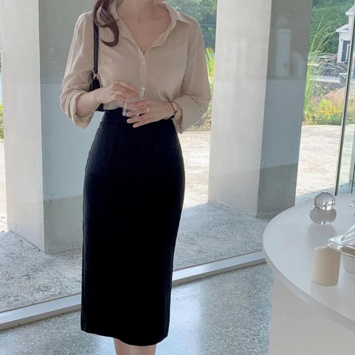 Woman wearing a long black pencil skirt and a fitted beige blouse.