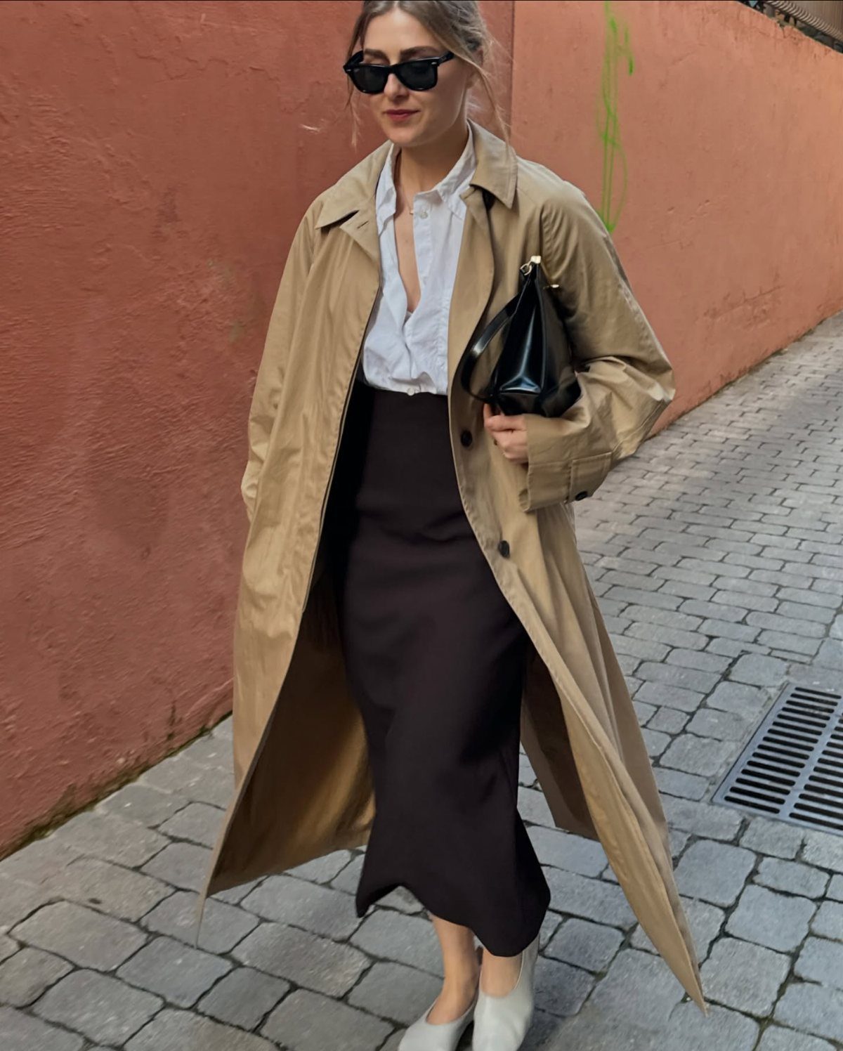 Woman in tan trench coat, white shirt, and long black pencil skirt.