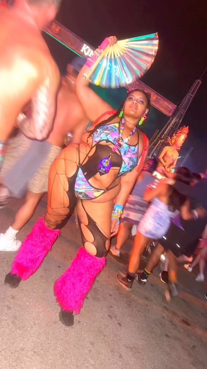 8 Plus Size Rave Outfits That Bring the Energy 3 Plus-size woman in colorful rave attire with pink leg warmers and rainbow fan.