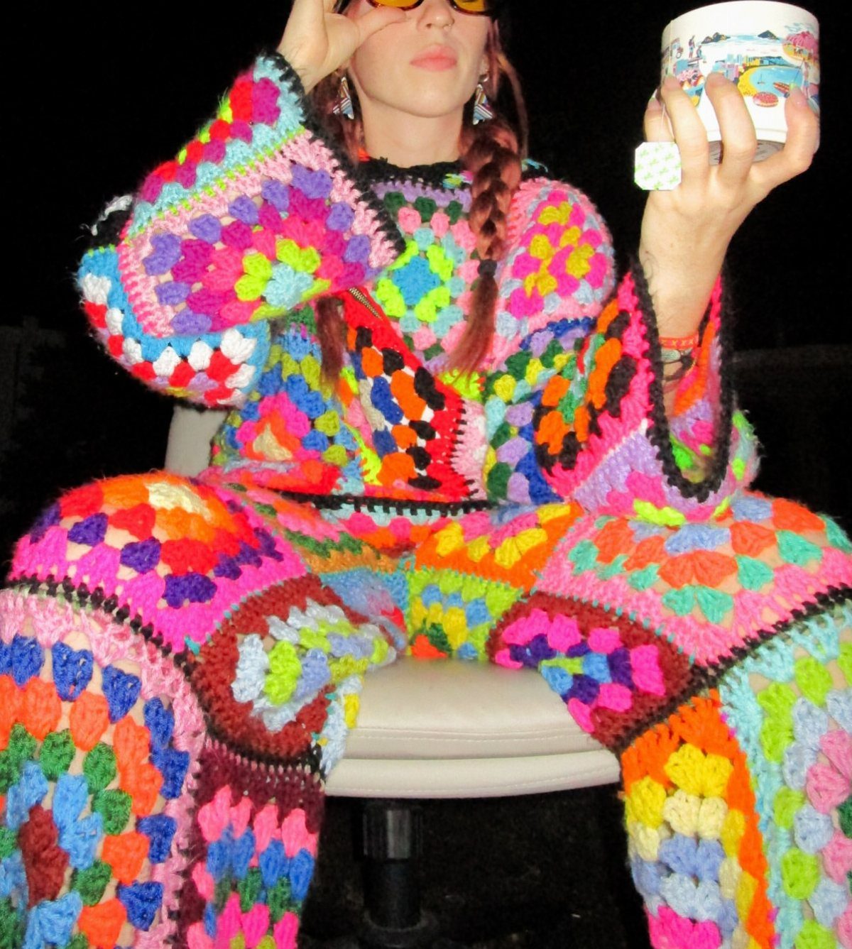 8 Plus Size Rave Outfits That Bring the Energy 8 Person wearing a colorful oversized crochet granny square outfit sitting in a chair