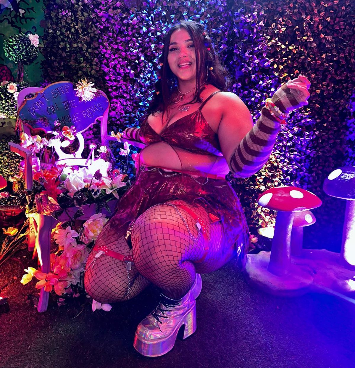 8 Plus Size Rave Outfits That Bring the Energy 5 Plus-size woman in metallic burgundy rave outfit and platform boots in neon setting.