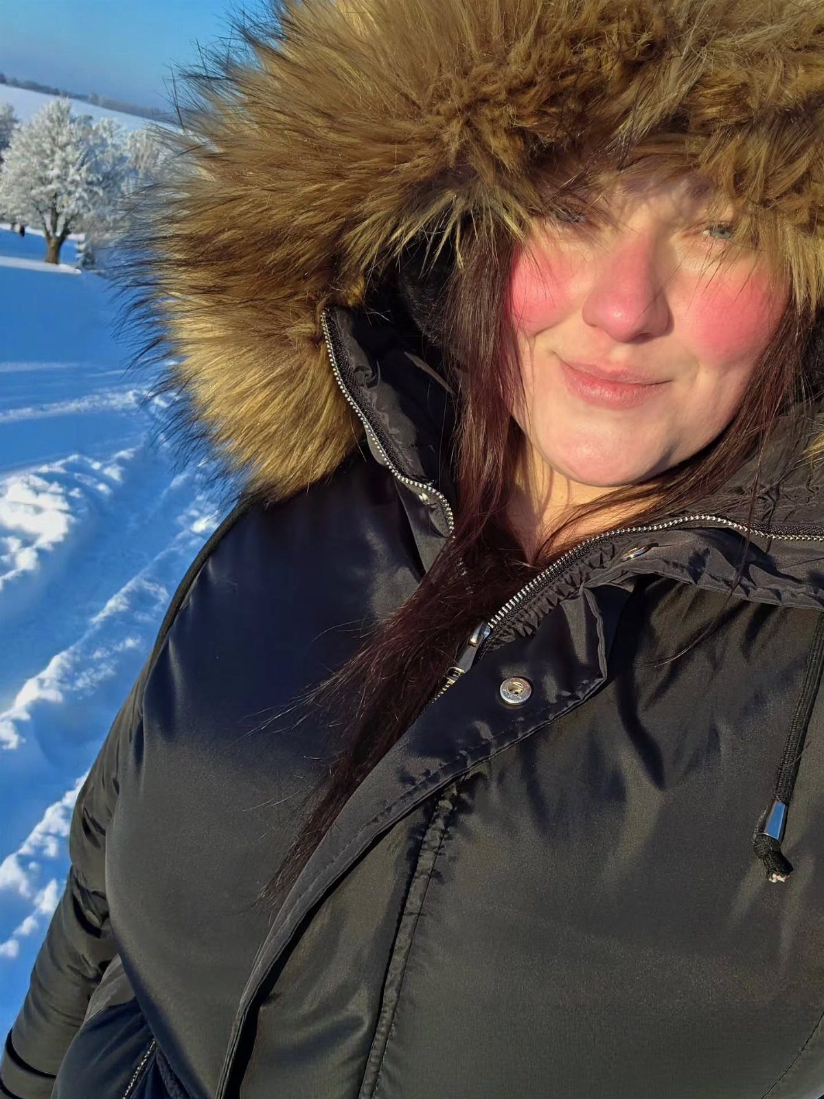 Plus Size Winter Outfits: 7 Cozy and Stylish Looks to Try 4 Woman in a black winter jacket with a fur hood in the snow.