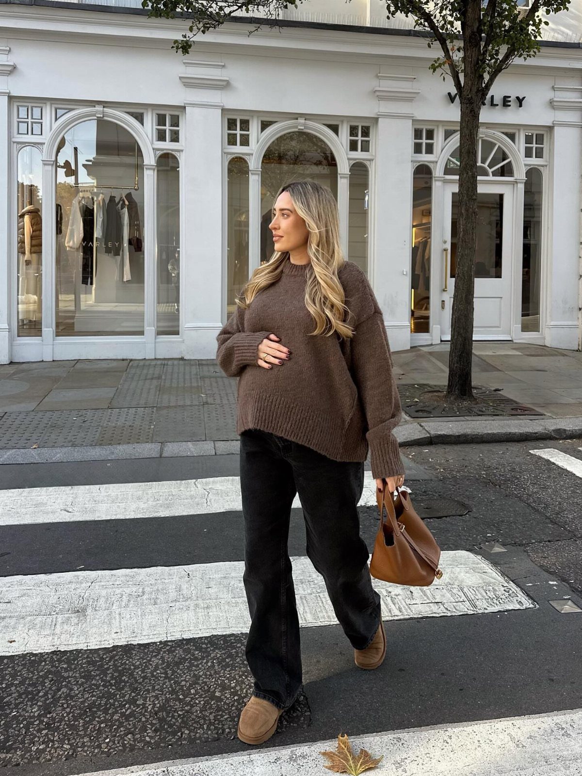 12 Pregnant Fall Outfits That Work Through Every Trimester 1 Pregnant woman wearing a brown oversized sweater and black wide-leg trousers on a city street.