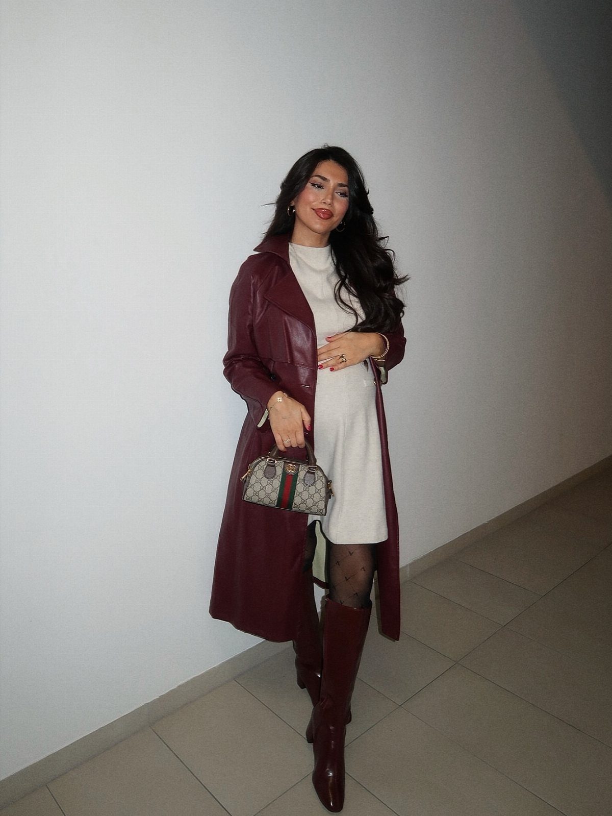 12 Pregnant Fall Outfits That Work Through Every Trimester 5 Pregnant woman in a short cream dress, burgundy leather coat, and tall burgundy boots.