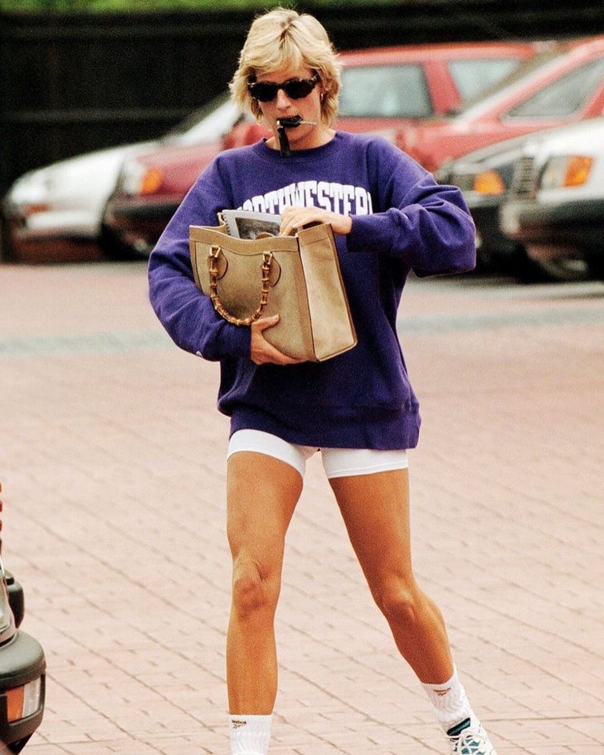 Princess Diana Outfits That Defined Royal Style (11 Ideas) 4 Princess Diana in a bold purple sweatshirt and white cycling shorts carrying a gold bag.
