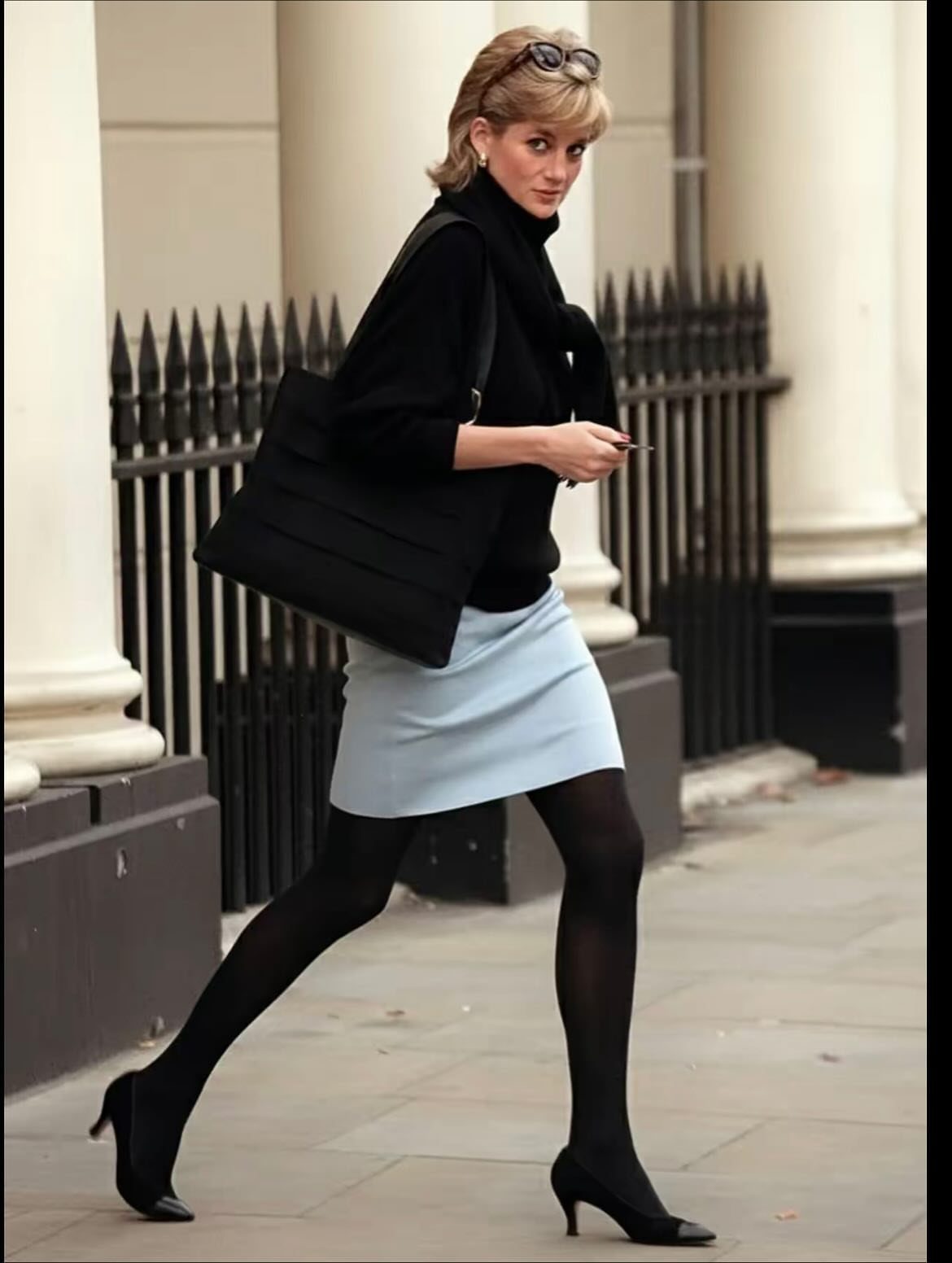 Princess Diana Outfits That Defined Royal Style (11 Ideas) 10 Princess Diana wearing a black turtleneck and light blue mini skirt walking outdoors.