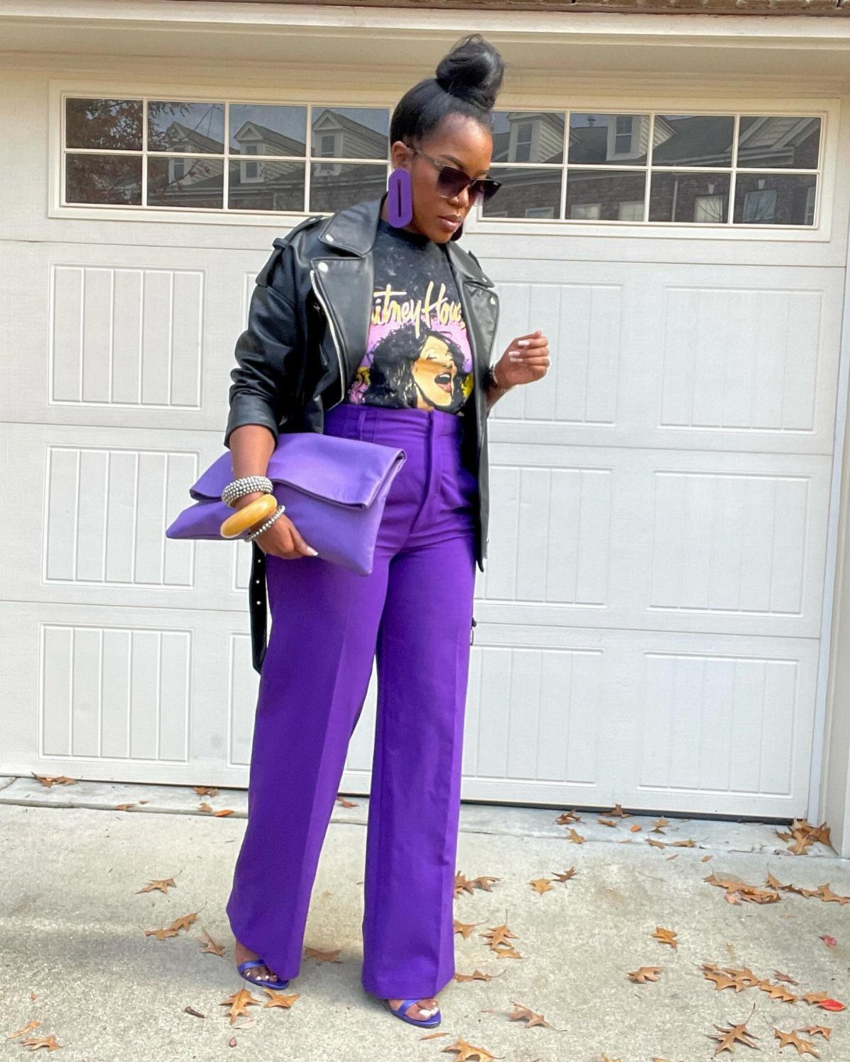 Purple Winter Outfits: 9 Ways to Style the Season's Boldest Color 5 Woman in purple wide-leg pants and a black leather jacket holding a purple clutch.