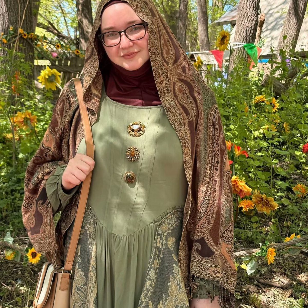 Renaissance Fair Outfits Women Can Wear: 12 Looks 1 Woman in a green Renaissance dress and patterned brown shawl among yellow sunflowers.