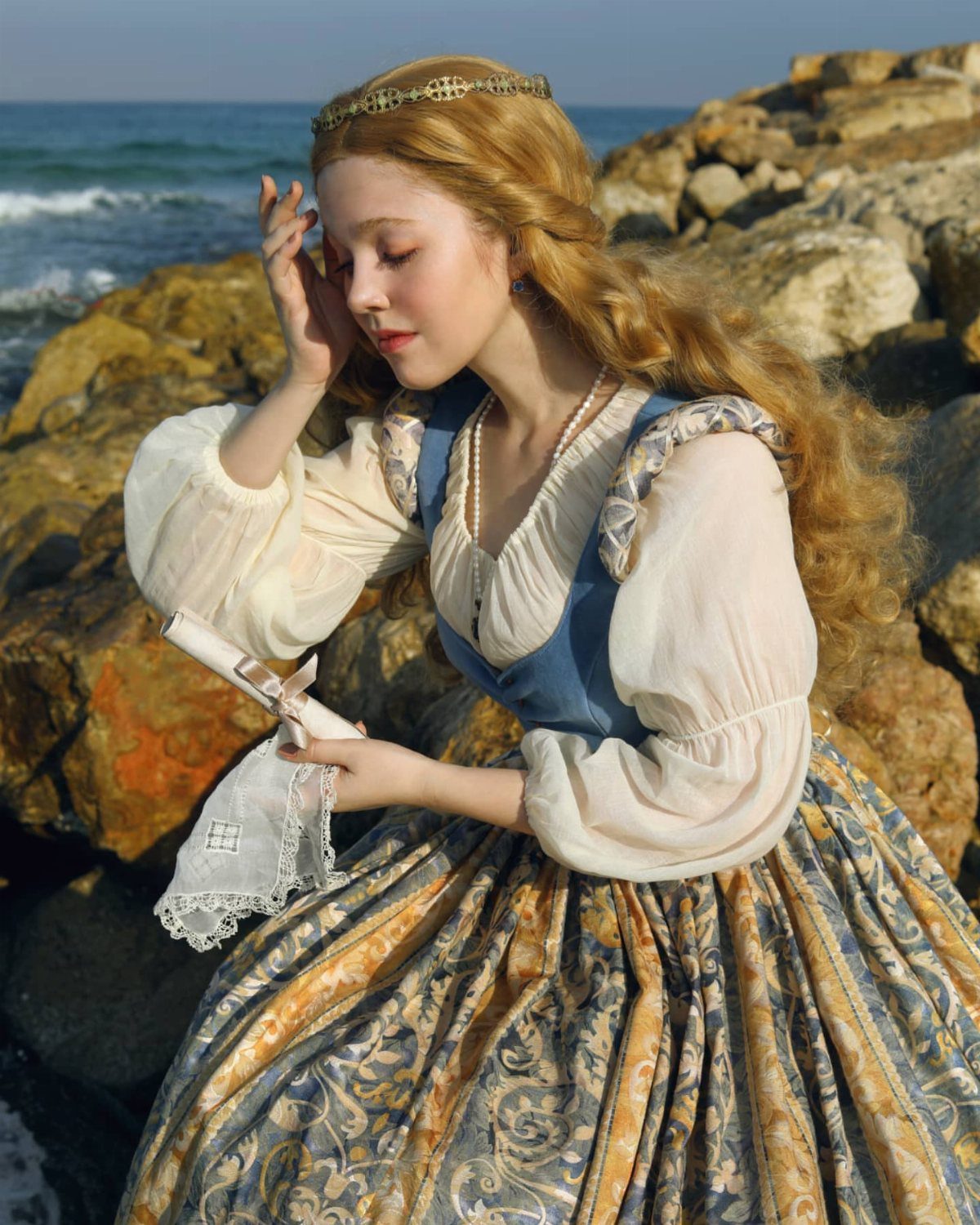 Renaissance Fair Outfits Women Can Wear: 12 Looks 8 Woman in royal renaissance attire with a gold crown sitting on seaside rocks.