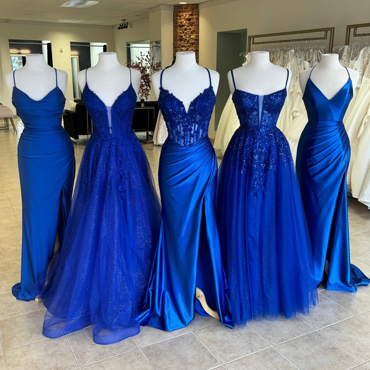 Royal Blue Outfits in 8 Styles for Every Occasion 3 Five royal blue gowns of various styles displayed on white mannequins in a shop.