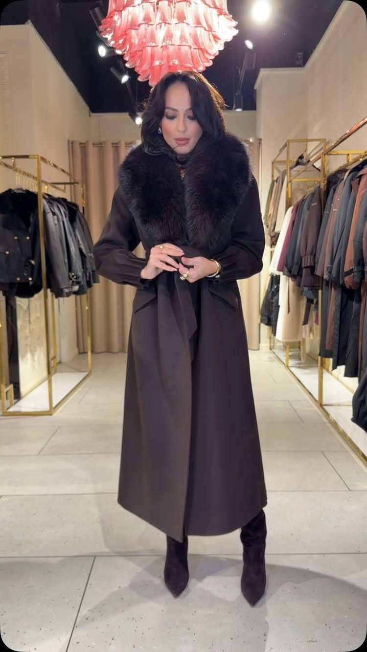 14 Serena van der Woodsen Outfits That Defined Gossip Girl Style 13 Woman in a long brown coat with fur collar standing in a boutique.