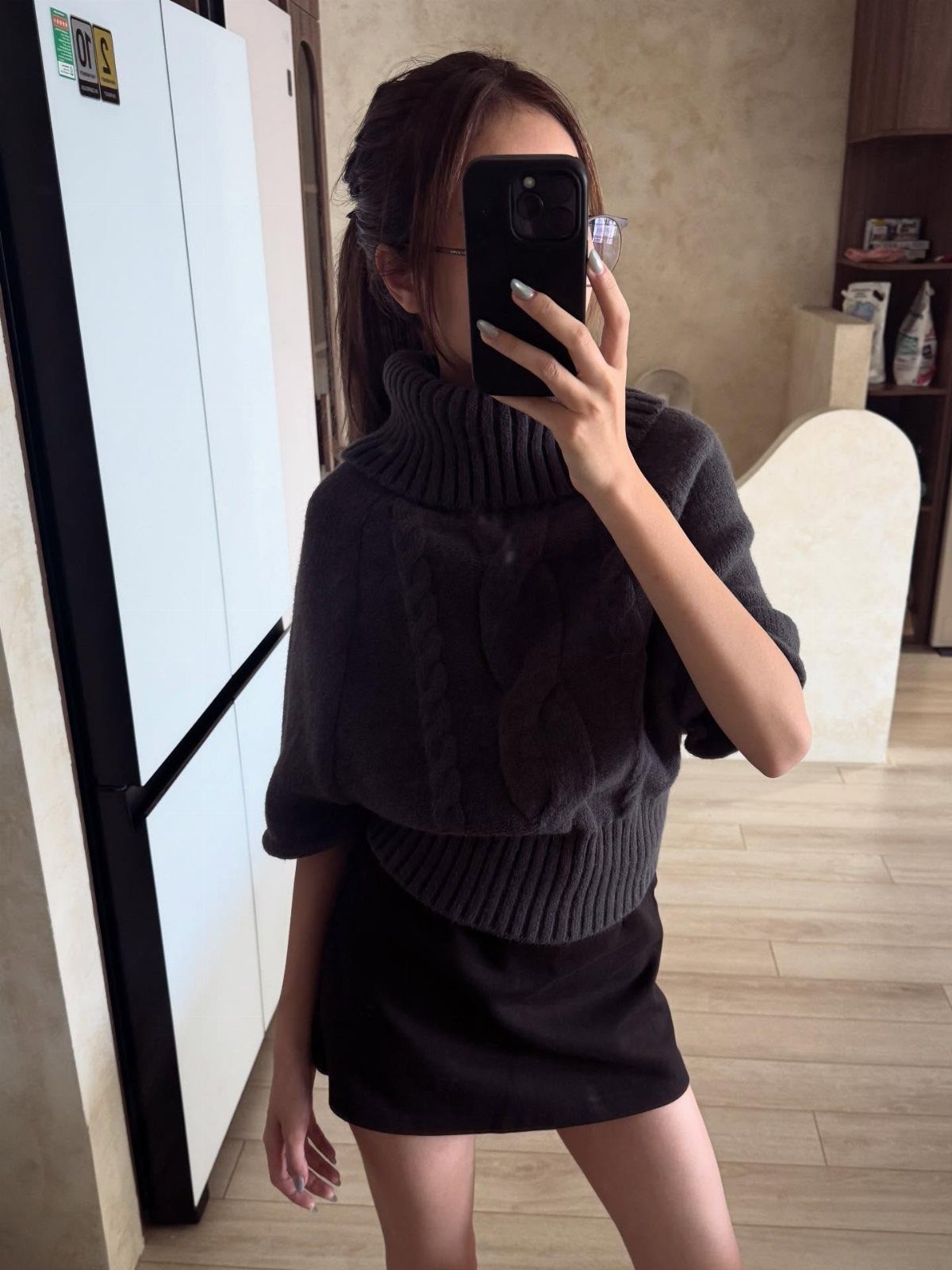14 Serena van der Woodsen Outfits That Defined Gossip Girl Style 9 Woman in oversized grey cable-knit sweater and black mini skirt taking a mirror selfie.