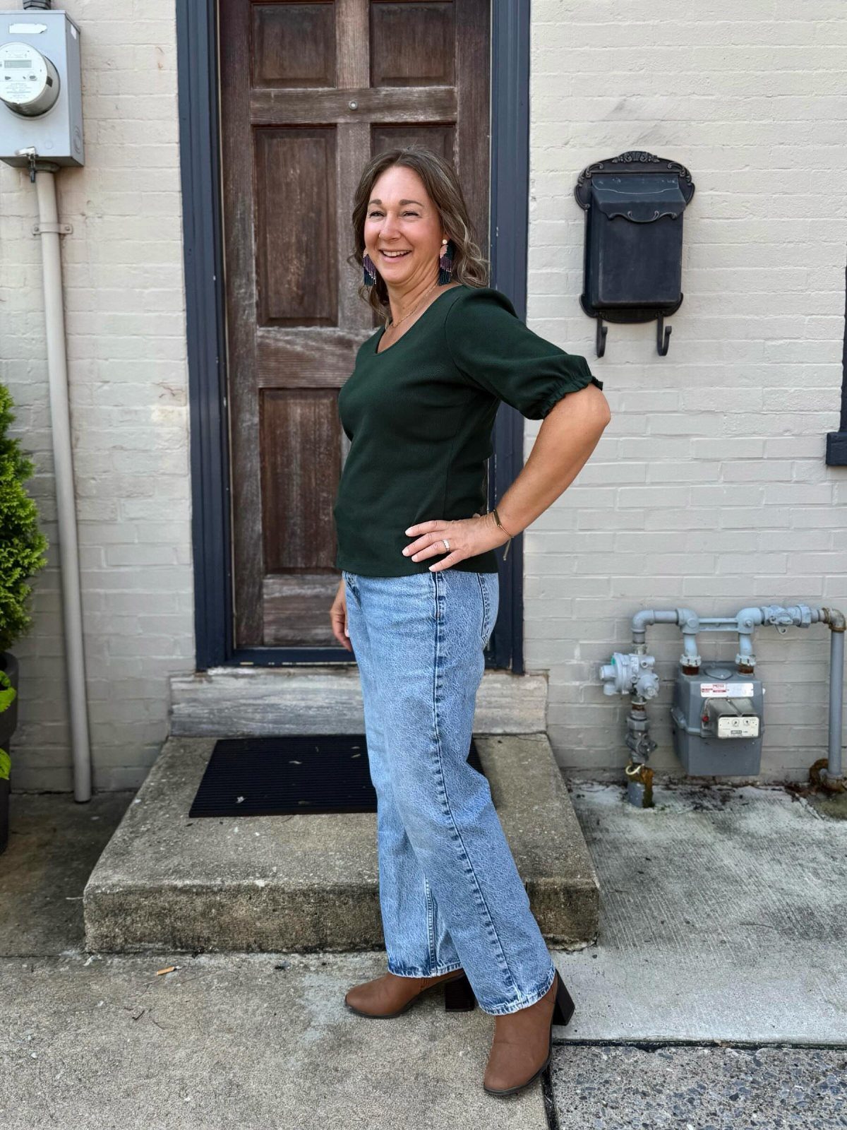 16 Short Torso Outfits That Balance Your Proportions 10 Woman wearing a dark green v-neck top and wide-leg light wash denim jeans.