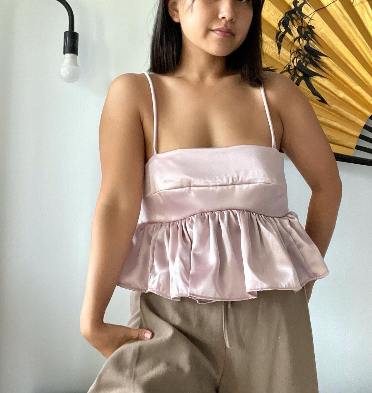 16 Short Torso Outfits That Balance Your Proportions 8 Woman wearing a pink satin peplum top and tan wide-leg trousers indoors.