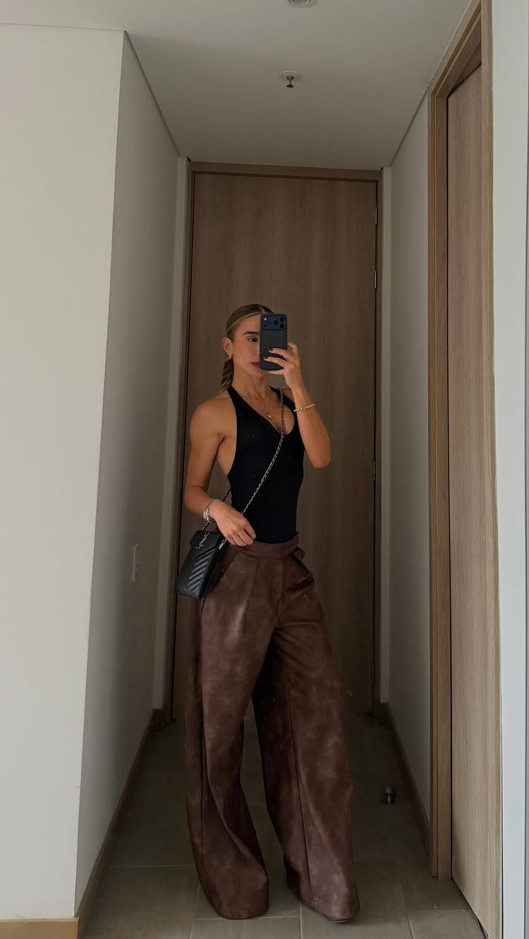 16 Short Torso Outfits That Balance Your Proportions 4 Woman wearing a black scoop neck bodysuit and brown wide-leg leather pants.