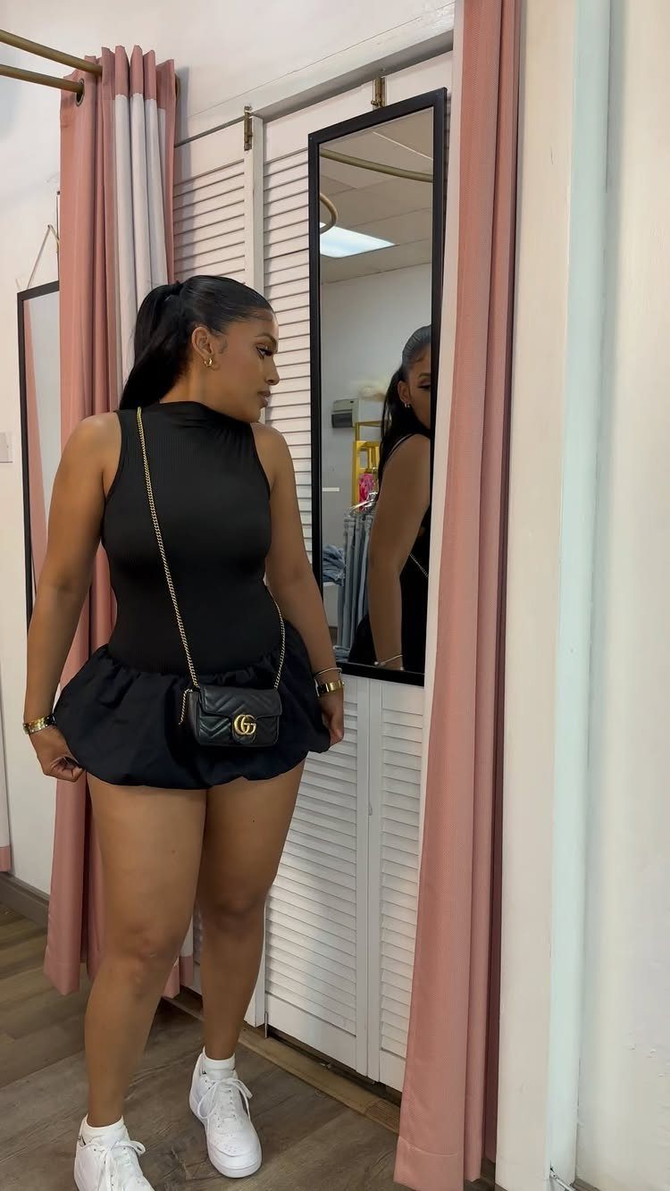 16 Short Torso Outfits That Balance Your Proportions 14 Woman in a black bodysuit and ruffled mini skirt posing in a dressing room.
