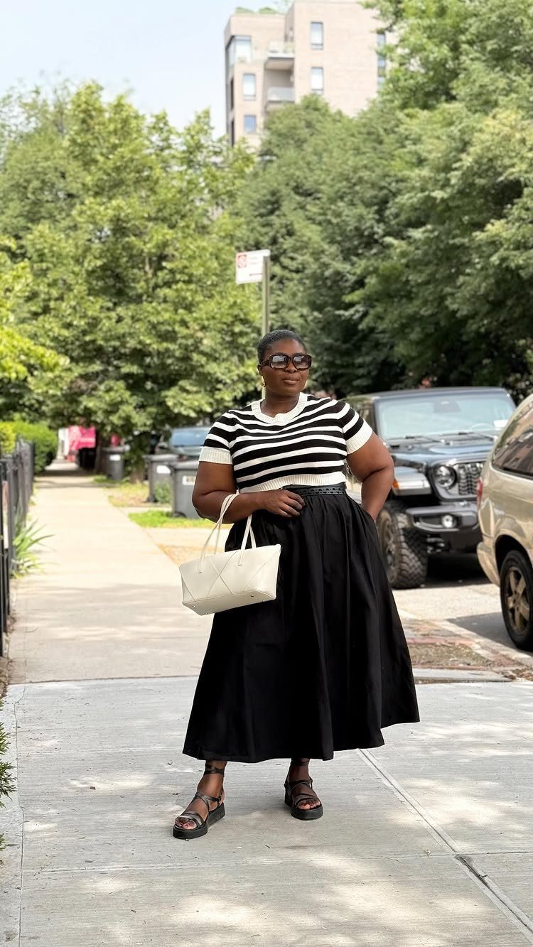 16 Short Torso Outfits That Balance Your Proportions 9 Woman wearing a striped t-shirt and black A-line midi skirt on a sidewalk.