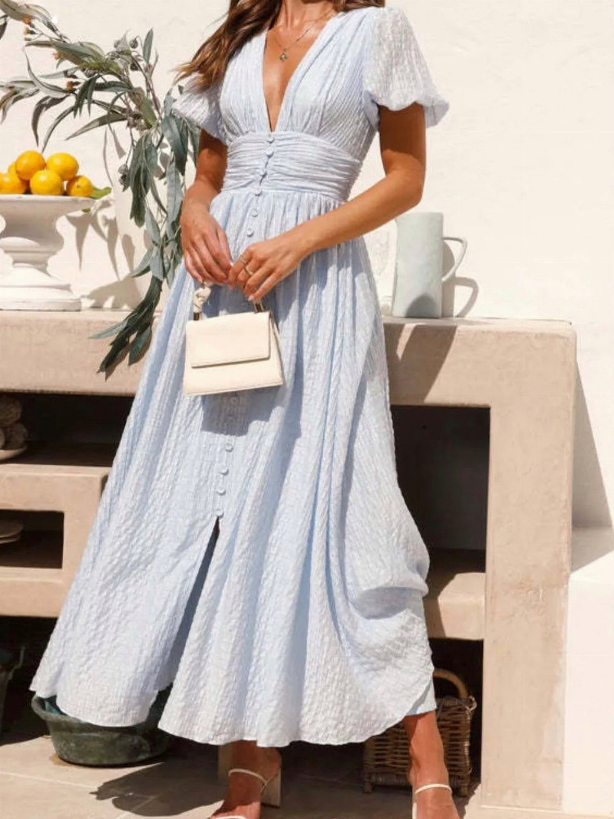 16 Short Torso Outfits That Balance Your Proportions 1 Woman in a light blue V-neck maxi dress holding a small white handbag.