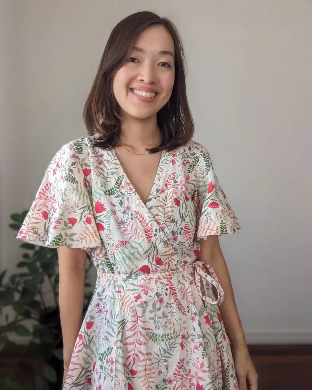 16 Short Torso Outfits That Balance Your Proportions 2 Woman wearing a white floral wrap dress with short flutter sleeves and a tie waist.