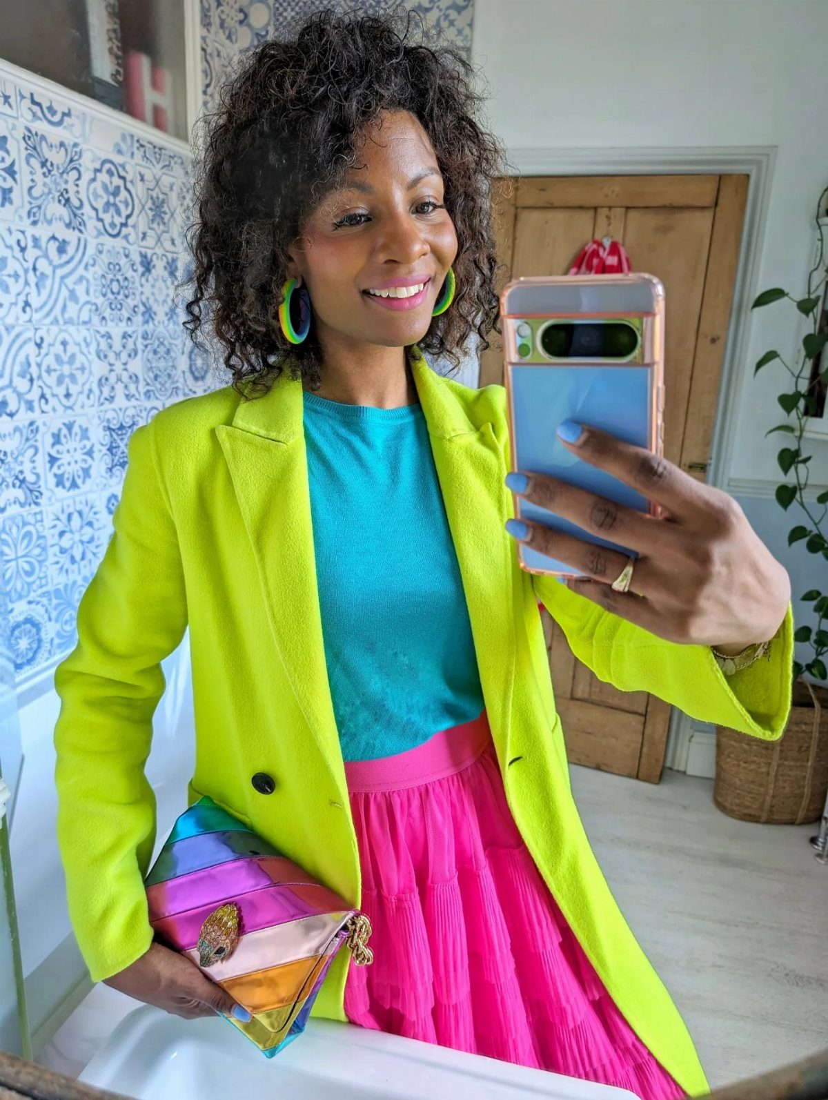 12 Spring Work Outfits That Work From Desk to Dinner 12 Woman wearing a neon yellow blazer, blue top, and pink pleated skirt for work.