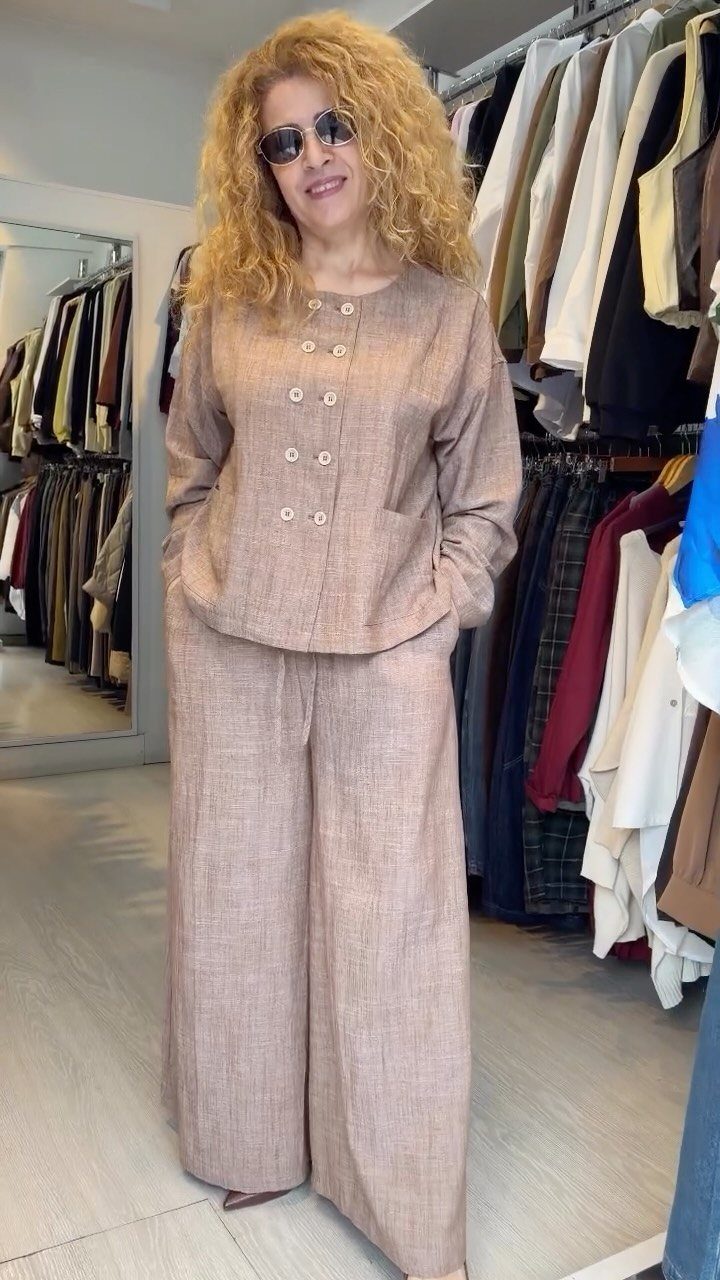 12 Spring Work Outfits That Work From Desk to Dinner 10 Woman in a light brown linen jacket and wide-leg trousers in a clothing store.