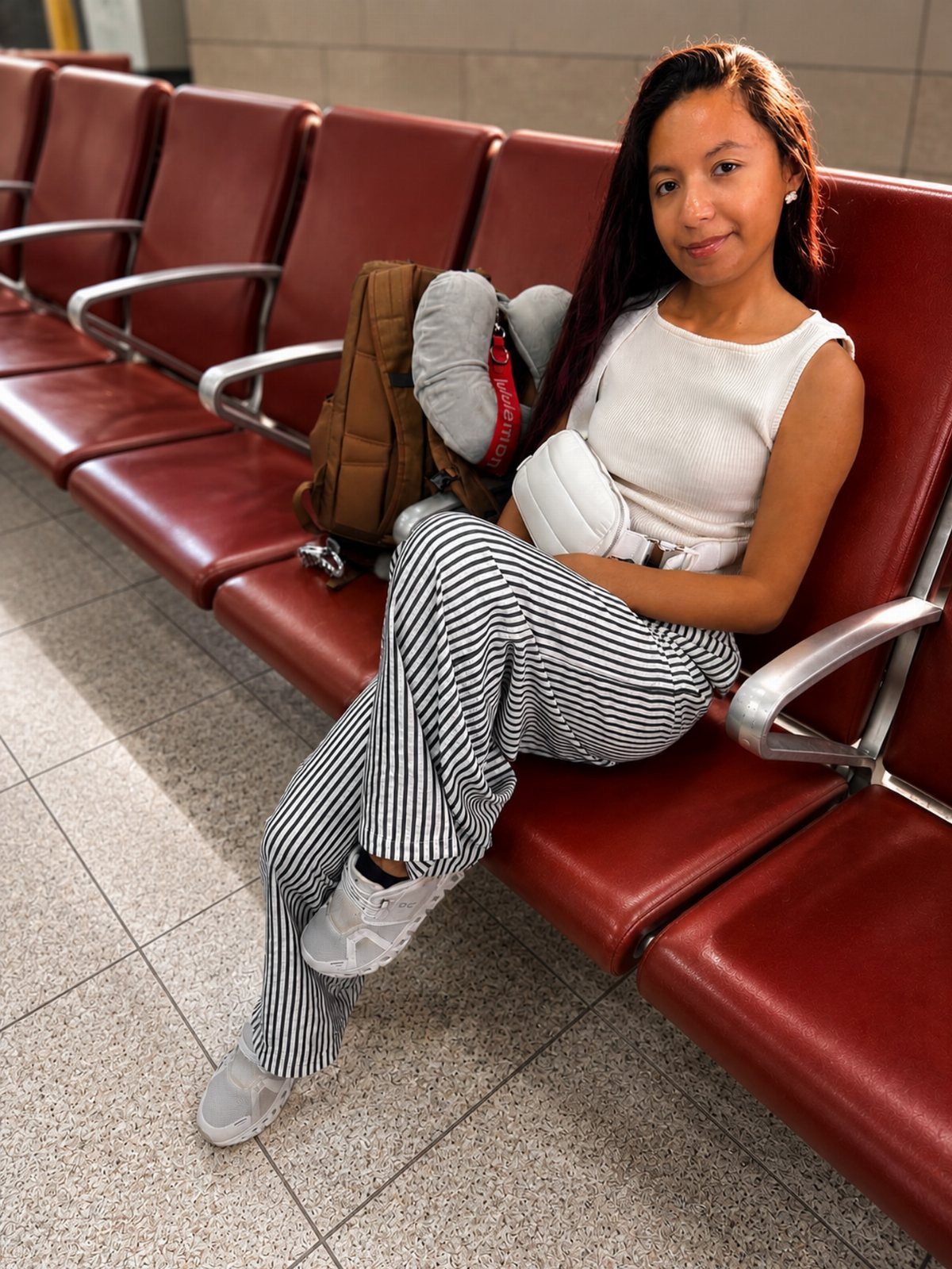 Woman in striped pants and white top sitting in red airport terminal seats.