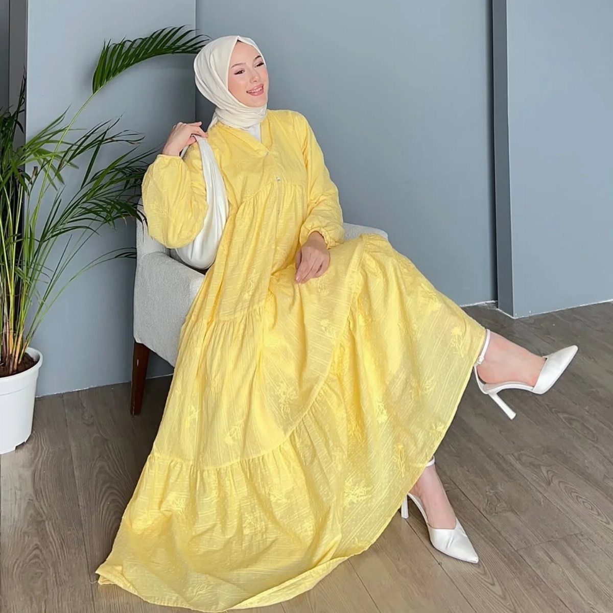 8 Summer Hijab Outfits for Modest, Breathable Style 1 Woman in white hijab and flowy yellow maxi dress sitting in a white chair.