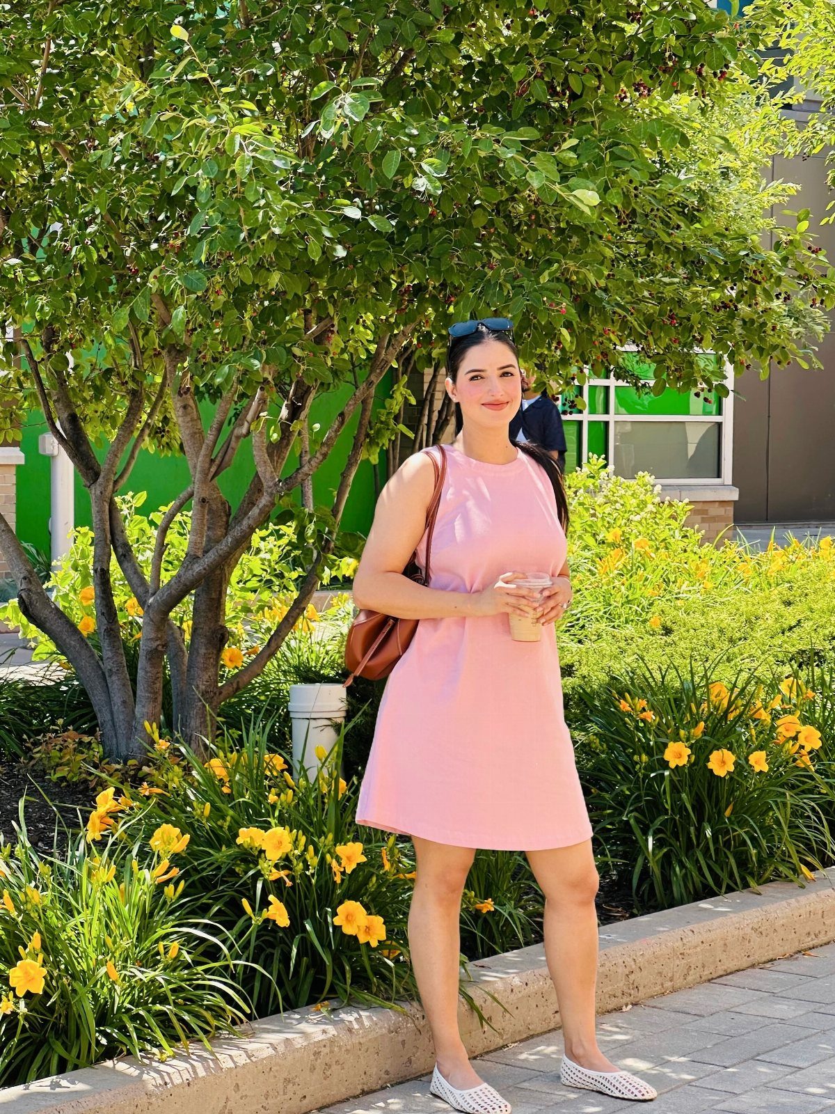 Summer House Outfits: 10 Effortless Ideas for Weekends Away 4 Woman in a sleeveless pink mini dress standing by a tree and yellow flowers.