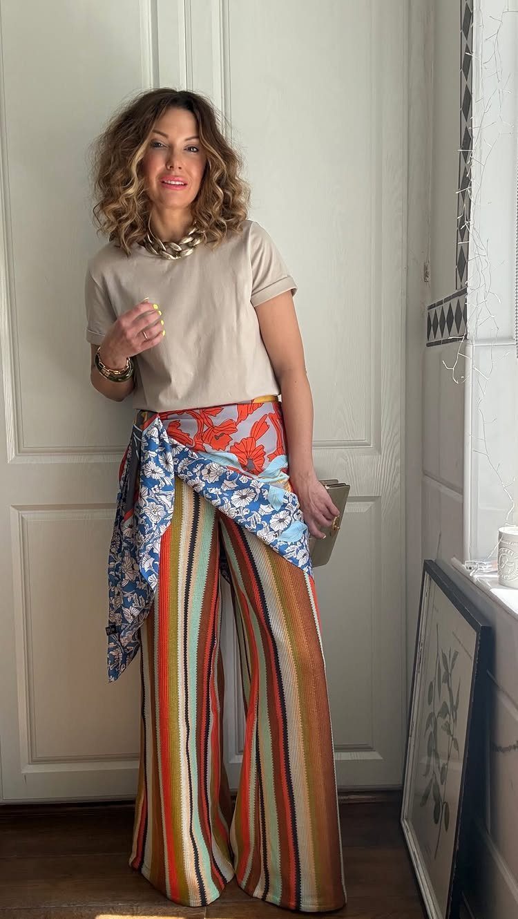 Summer House Outfits: 10 Effortless Ideas for Weekends Away 9 Woman wearing a beige t-shirt, striped trousers, and a chunky gold chain necklace.