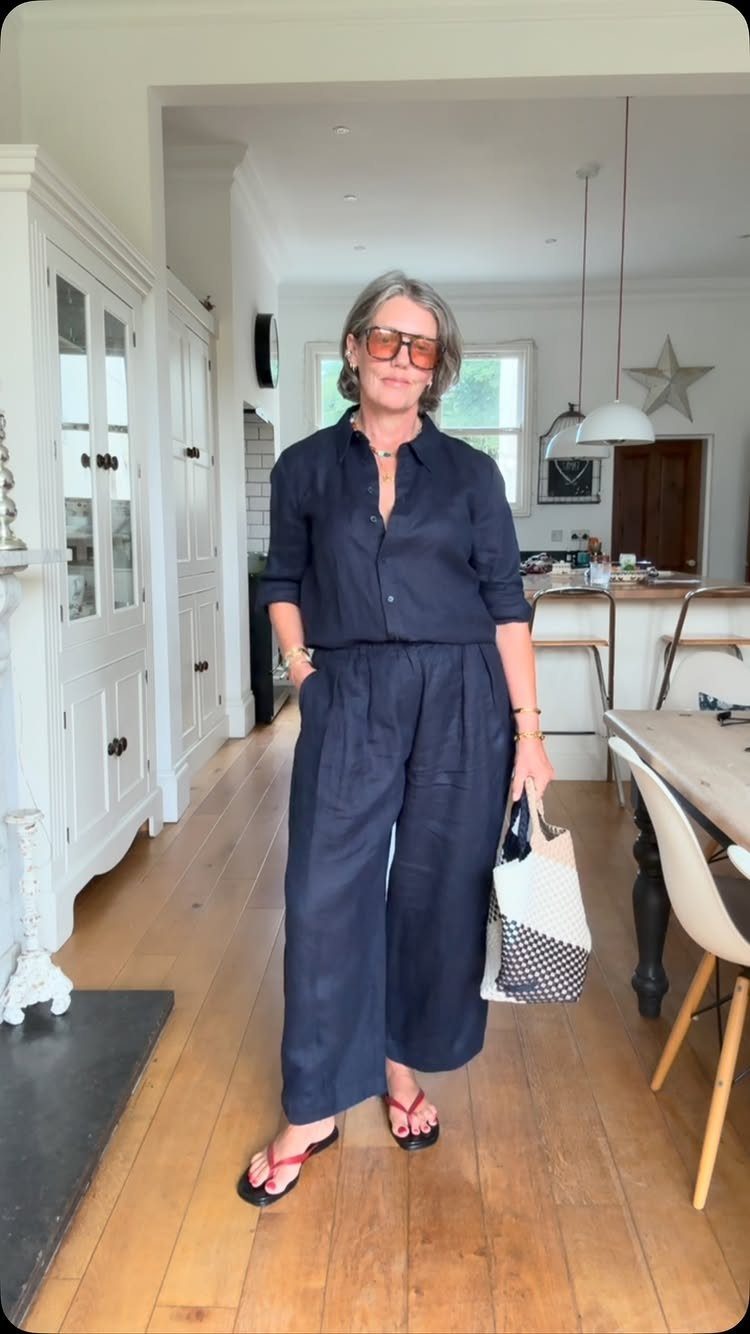 9 Summer Vacation Outfits to Pack for Your Next Trip 4 Woman in navy blue linen top and wide-leg pants holding a patterned tote bag.