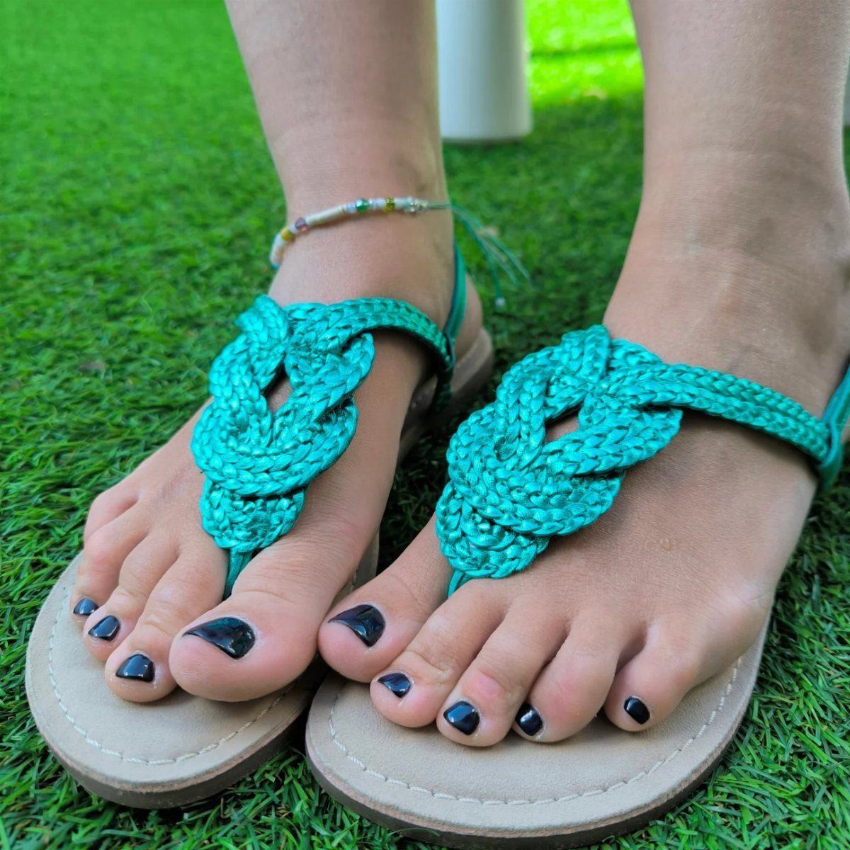 9 Summer Vacation Outfits to Pack for Your Next Trip 9 Teal braided strappy sandals on feet with black nail polish standing on green grass
