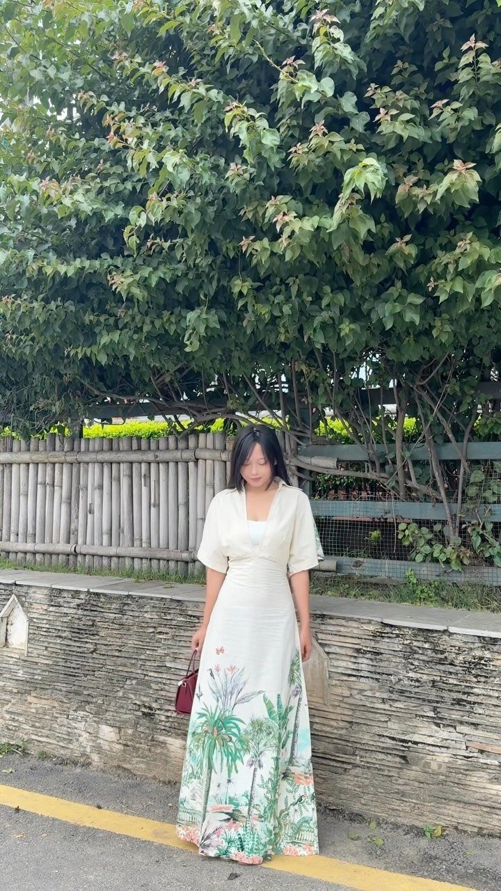 9 Summer Vacation Outfits to Pack for Your Next Trip 2 Woman wearing a white maxi dress with a tropical palm tree print on the skirt.