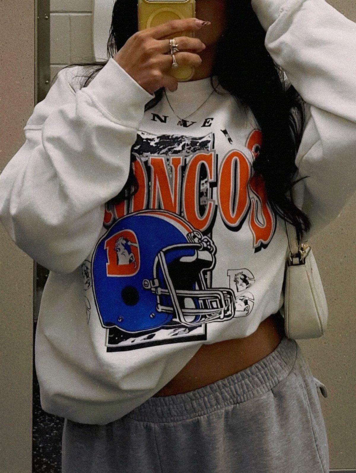12 Super Bowl Outfits From Sporty to Sequined for Game Day 11 Person wearing a white Denver Broncos graphic sweatshirt and grey sweatpants.